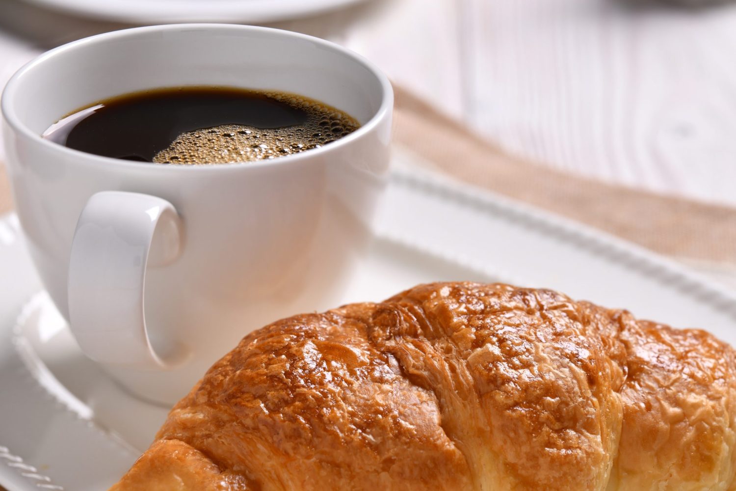A cup of coffee and croissant on wooden table A cup of coffee and croissant on wooden table